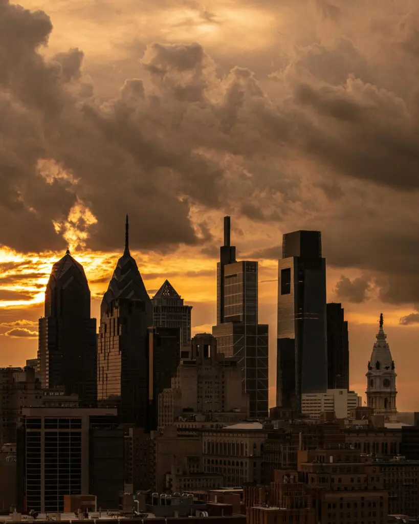 Dramatic sunset over Philadelphia skyline with iconic skyscrapers silhouetted against a cloudy sky.